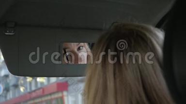年轻迷人的女人在车里<strong>画眉</strong>毛，看着后视镜。 慢动作