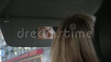 年轻迷人的女人在车里画眉毛，看着后视镜。 慢动作
