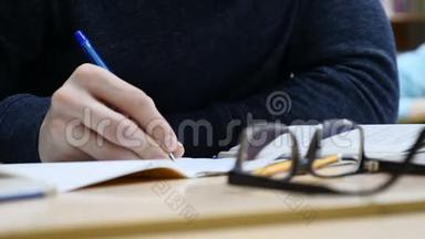 在记者招待会上`男记者的手握着笔做笔记. 看着桌子上的眼镜。