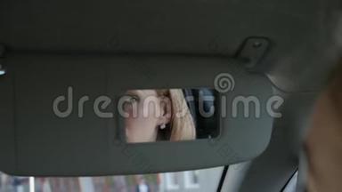 年轻迷人的女人正在车里化妆，看着后视镜。 慢动作