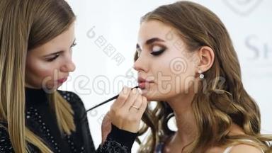 化妆师将口红涂在令人惊叹的时尚模特脸上。 漂亮的女人脸，用刷子做的完美妆容