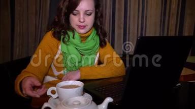 年轻漂亮的<strong>女孩</strong>坐在咖啡馆的桌子上，喜欢笔记本电脑。 <strong>女孩</strong>拿着杯子<strong>喝茶</strong>。 她微笑着