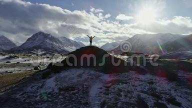 攀登雪峰的男子用冰锥举起双手。 登山者举起双手站在岩石的顶端