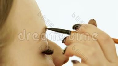 在美容工作室化妆眉毛时，闭上女人的脸。 女人用化妆刷在眉毛上着色