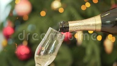 特写香槟倒入酒杯，背景上的圣诞树。 将香槟倒入玻璃的特写镜头