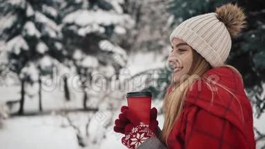 年轻漂亮的女孩穿着暖和的衣服站在圣诞树旁边，在雪地里喝着报纸上的<strong>热饮料</strong>