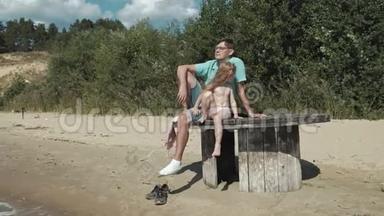 父亲和小女儿正坐在河岸海滩上的一个木台阶上