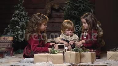 两个穿着裙子的<strong>女孩和</strong>一个金发小男孩在一个舒适的房间里坐在多达克<strong>和圣诞树</strong>之间玩耍