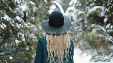 从后面看着戴着绿色帽子和外套的女士在冬天的森林里走来走去。 女孩看着镜头摆姿势