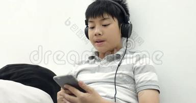 一个快乐<strong>的</strong>亚洲青少年<strong>男孩</strong>躺在清醒<strong>的</strong>智能手机和耳机和<strong>听音乐</strong>在家里<strong>的</strong>肖像。