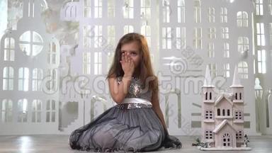一个穿着灰色<strong>闪</strong>亮裙子的可爱女孩坐在玩具宫附近，<strong>送</strong>上一个飞吻，一张贺卡。慢镜头拍摄