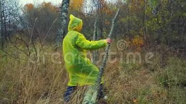一个穿着雨衣的女人在森林里的一棵倒下的树上台阶。 总体计划。