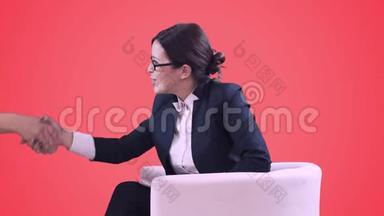 电视演播室。 戴眼镜的深色头发。 她穿着西装坐在工作室里接受采访。 红色背景。