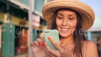 年轻的无忧无虑的快乐嬉皮士女人在老旧建筑使用移动电话的草帽混合种族旅游女孩