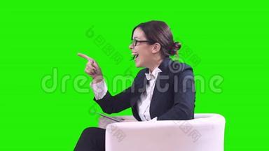 电视演播室。 戴眼镜的深色头发。 她穿着西装坐在工作室里接受采访。 绿色