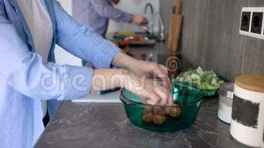 女人正在把西红柿和黄瓜切在白色塑料切割板上，然后把它放进沙拉碗里