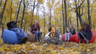 深色皮肤和白色的男人，三个女人坐在秋天森林里的火炉旁，用<strong>热水</strong>瓶慢慢地<strong>喝</strong>