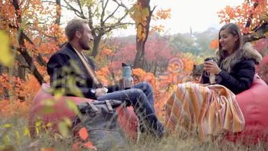 在秋天的森林里，一对情侣坐在泡芙上，他们用热水瓶喝酒，交流，慢动作