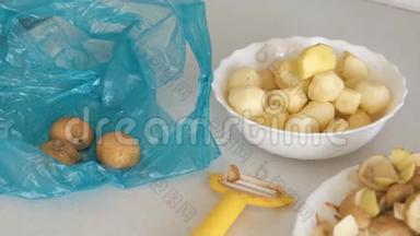 盘子里的小土豆，厨房桌子上的果皮和剥皮机。 塑料蓝色袋子上的未剥皮土豆。