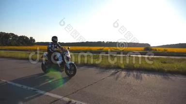 摩托车手驾驶摩托车在乡间小路上，背景是向日葵田。 戴头盔的年轻人