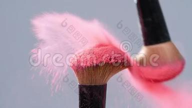 化妆刷与粉红色粉末溅在灰色背景爆炸慢动作
