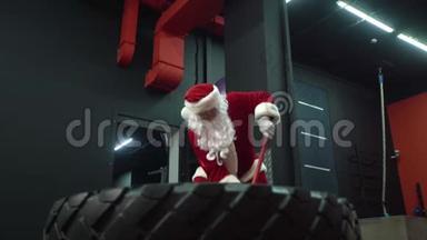 圣诞老人在健身房训练圣诞节。 圣诞老人用<strong>锤子敲打</strong>车轮轮胎。