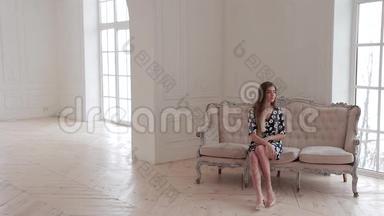 时装模特在摄影棚里摆姿势坐在优雅的沙发上