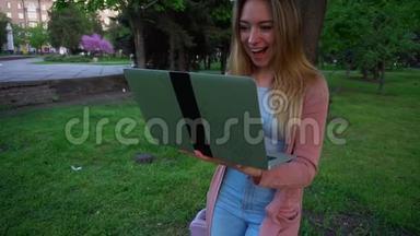 女孩在斯普里格公园里用笔记本电脑聊天，慢慢地靠在树上，脸上<strong>露出</strong>满意的表情。