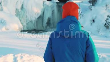 一个年轻的女孩拍了一张<strong>冰冻</strong>瀑布的照片，在智能手机上拍照。 水流，浮冰和冰柱，