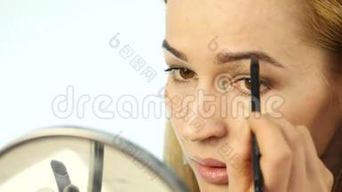 美丽的女人在小镜子前<strong>画眉</strong>毛，用化妆刷做日常化妆。 4K