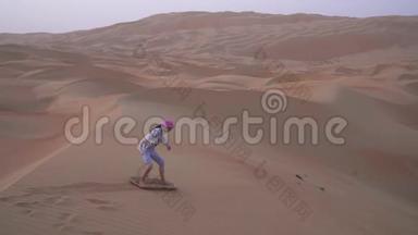 在阿拉伯联合酋长国的Rubal Khali沙漠中的沙丘坡上，少女在沙板上翻滚