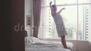 幸福的年轻女人在现代卧室的床上从窗户上看到城市的景色。 慢动作。 1920x1080