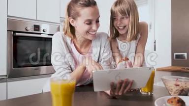 漂亮的年轻母亲和女儿在家厨房吃早餐时使用数码平板电脑