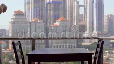年轻的女家庭教师在阳台上准备早餐，俯瞰市中心的摩天大楼