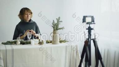 有魅力的、开朗的女人坐在桌子旁，在视频博客上录制关于相机桌面设计的视频