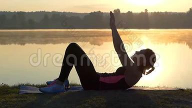 苗条的女人躺在湖边，日落时抬起头
