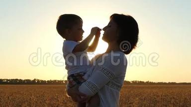 一位快乐的母亲在夕阳的背景下把孩子抱在麦田的怀里。 快乐的孩子抚摸他