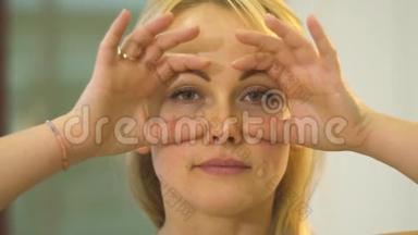 从眼睛周围的皱纹中锻炼，女人把手放在脸上，睁开眼睛