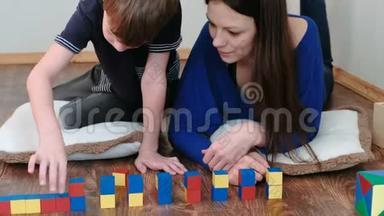 用积木和立方体建造塔楼。 妈妈和儿子一起玩着木制的彩色教育玩具积木