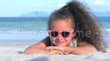 <strong>粉色</strong>眼镜中美丽的小女孩的特写镜头，可爱的<strong>微</strong>笑看着镜头，躺在沙滩上