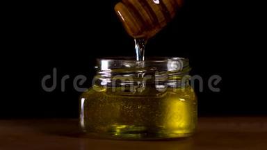 蜂蜜从黑色背景的蜂蜜勺上滴下。健康的有机浓蜂蜜，从木制的蜜匙中蘸取。。