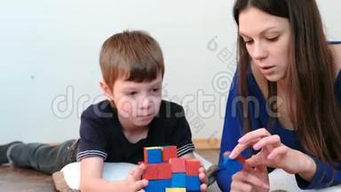 用积木和立方体建造塔楼。 妈妈和儿子一起玩着木制的彩色教育玩具积木