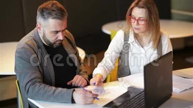 几个同事在办公室一起工作。 两名商务人员在笔记本电脑上准备新项目。 他们写下了