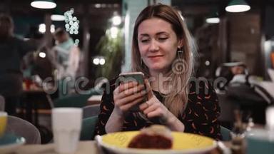 一个年轻女孩在餐馆里用手机。 桌子上有一个餐厅里的甜点，<strong>一把</strong>叉子和<strong>一把</strong>刀。