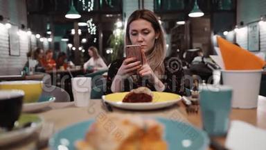 一个年轻女孩在餐馆里用手机。 桌子上有一个餐厅里的甜点，一把叉子和一把刀。