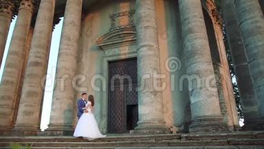 可爱的新婚夫妇站在远离镜头的城堡附近。 慢慢地