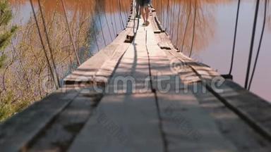 一家人妈妈、爸爸和女儿的特写腿走在河上的旧吊桥上。
