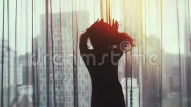 年轻漂亮的黑发女人跑到窗户前，揭开窗帘，欣赏着家中窗户上的日落景色