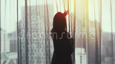 年轻漂亮的深褐色头发的女人，打开的头发，站在窗边喝着咖啡，欣赏着家中窗外的景色