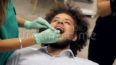 一位牙医检查一位年轻人的牙齿，牙医助理正在写应该修理的东西